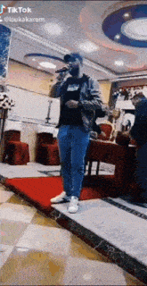 a man is singing into a microphone while standing on a stage in a room .
