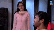 a woman in a pink dress stands next to a man in a yellow shirt with a z on the bottom