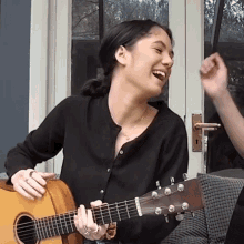 a woman in a black shirt is playing a guitar and laughing