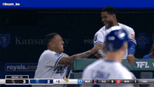 two baseball players are shaking hands in a dugout with a kansas city ad behind them