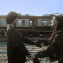 two women are holding hands in front of a train and one has a star on her arm
