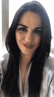 a woman with long dark hair and red lipstick smiles