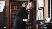 a man in a suit is pouring coffee into a cup with the nbc logo on the bottom