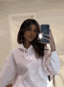a woman in a pink hoodie is taking a selfie with her phone .