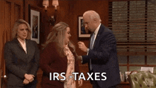 a man in a suit and tie is standing next to two women in a room and says `` irs taxes '' .