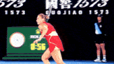 a woman in a red dress is playing tennis in front of a rolex advertisement