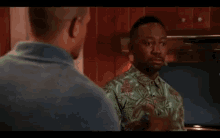a man in a green shirt is pointing at another man in a kitchen .