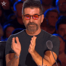 a man wearing glasses and a black shirt applauds in front of a crowd
