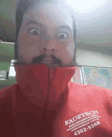 a man with a beard and mustache is wearing a red jacket that says kadetech .
