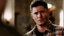 a man in a plaid shirt is looking at another man in a room .