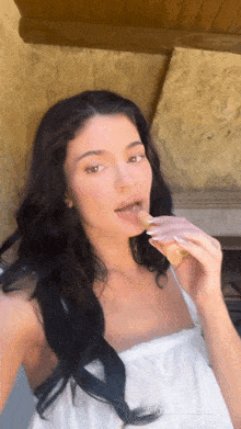 a woman in a white dress is taking a selfie while eating a piece of food .