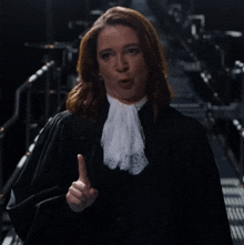 a woman in a black robe with a white lace tie is giving a thumbs up