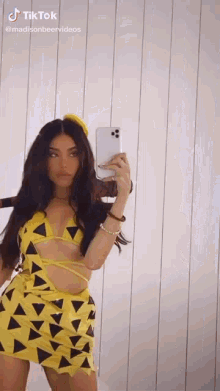 a woman is taking a selfie with her phone while wearing a yellow and black dress .