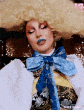 a drag queen wearing a wig and a blue scarf .