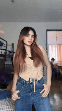 a woman in a tan top and blue jeans is standing in a room