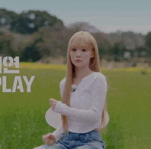 a woman in a white shirt is standing in a field with the word play behind her