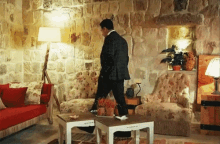 a man in a suit walks through a living room with a stone wall