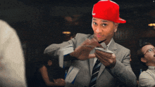 a man wearing a red hat and a suit holds a piece of paper