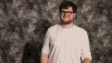 a man wearing glasses and a white shirt stands in front of a gray wall