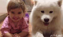 a little girl is laying on the floor next to a white dog ..