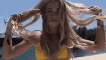 a woman in a yellow bikini is holding her hair in her hands