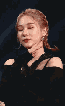 a close up of a woman 's face with her hand on her chin . she is wearing a black top and earrings .