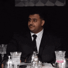 a man in a suit and tie is sitting at a table with glasses
