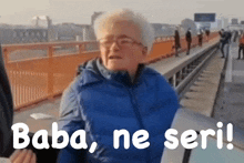 an older woman in a blue jacket is standing on a bridge with the words baba ne seri written below her