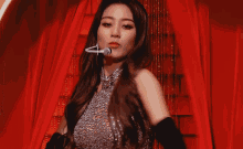 a woman in a silver dress and black gloves is standing in a red curtain .