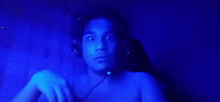 a shirtless man wearing headphones and a microphone in a blue light