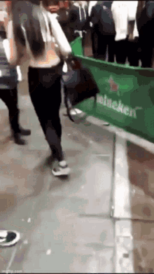 a woman is walking past a heineken banner on the sidewalk