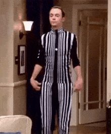a man is standing in a living room wearing a black and white striped jumpsuit .