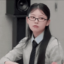 a young woman wearing glasses and a tie is sitting at a desk .