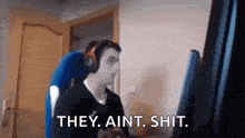a man wearing headphones is sitting in front of a computer screen and saying `` they ain 't shit '' .