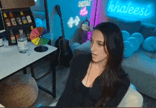 a woman sits on a couch in front of a khaleesi neon sign