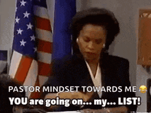 a woman in a suit is sitting at a desk in front of an american flag and talking on a cell phone .