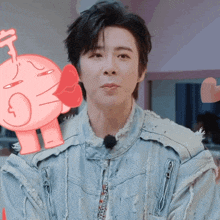 a man wearing a denim jacket has a pink cartoon character behind him with a heart on it