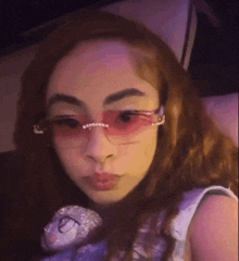 a girl wearing pink sunglasses is holding a stuffed animal .
