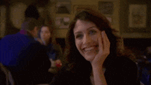 a woman is smiling while sitting at a table with her hand on her chin .