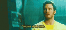 a man in a yellow shirt is standing in a dark room and saying `` you 're welcome . ''