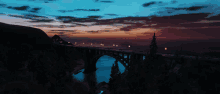 a bridge over a body of water at night with a sunset in the background