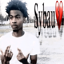a young man giving the middle finger in front of a sign that says sybau