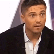 a man in a suit and white shirt is making a surprised face while sitting on a couch .