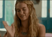 a woman with long blonde hair and a butterfly necklace is smiling .