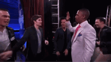 a man in a white suit and red tie is giving a high five to another man
