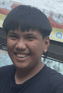 a young boy smiles in front of a sign that says q.