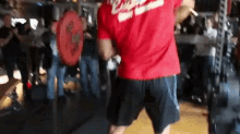 a man in a red shirt and black shorts is standing in a gym .