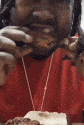 a man in a red shirt is smoking a cigarette and eating food