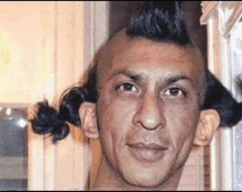a man with a mohawk and two buns on his head is smiling for the camera .