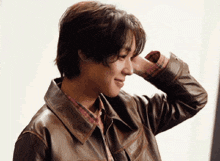 a man wearing a brown leather jacket holds his hand to his head